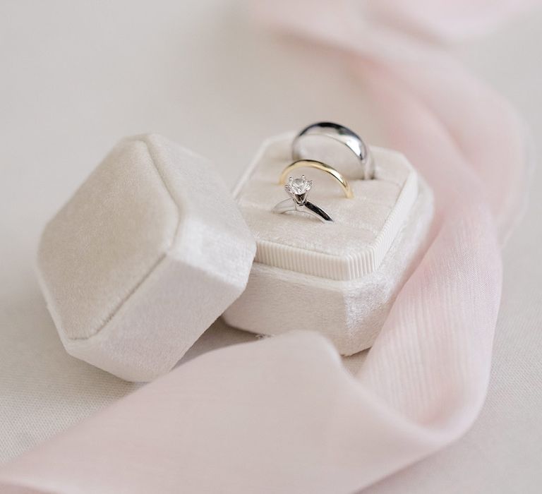 Wedding rings sit in white velvet box beside pink fabric 