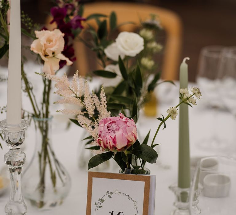 Book with table number rests on small vase filled with florals on white tablecloth 