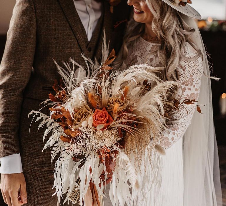 Bride in boho lace wedding dress holding a pampas grass, dried flowers and rose wedding bouquet 