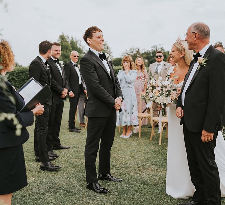 Groom in black tie greets the bride after she walked up the aisle with her father 