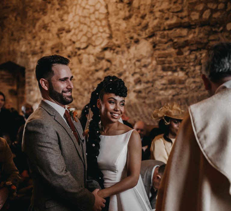 Groom in tartan three piece suit marries his bride wearing classic satin wedding dress during Christian ceremony at the Pentney Abbey