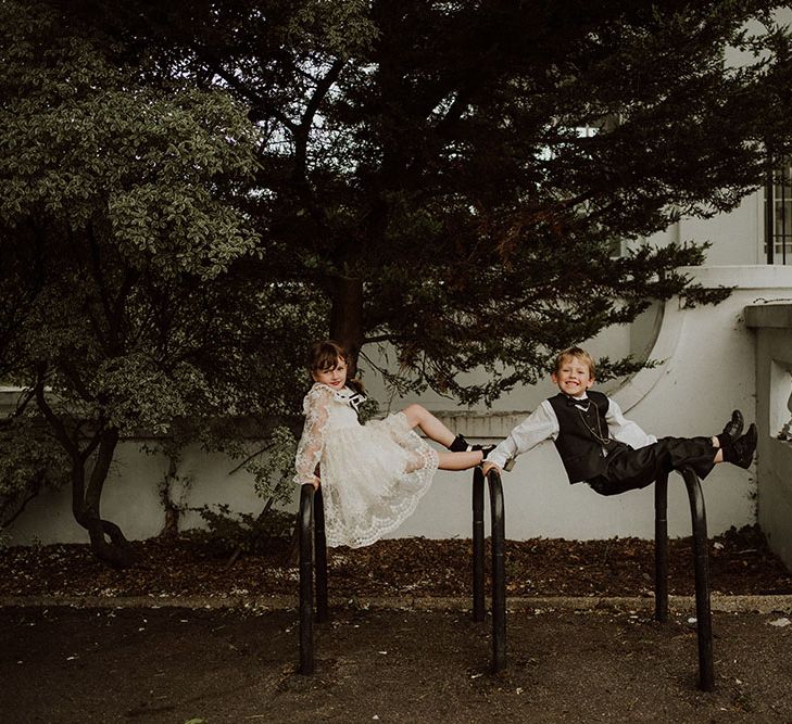 Flower girl in lace dress with black ribbon and page boy play outdoors at Belair House during wedding reception 