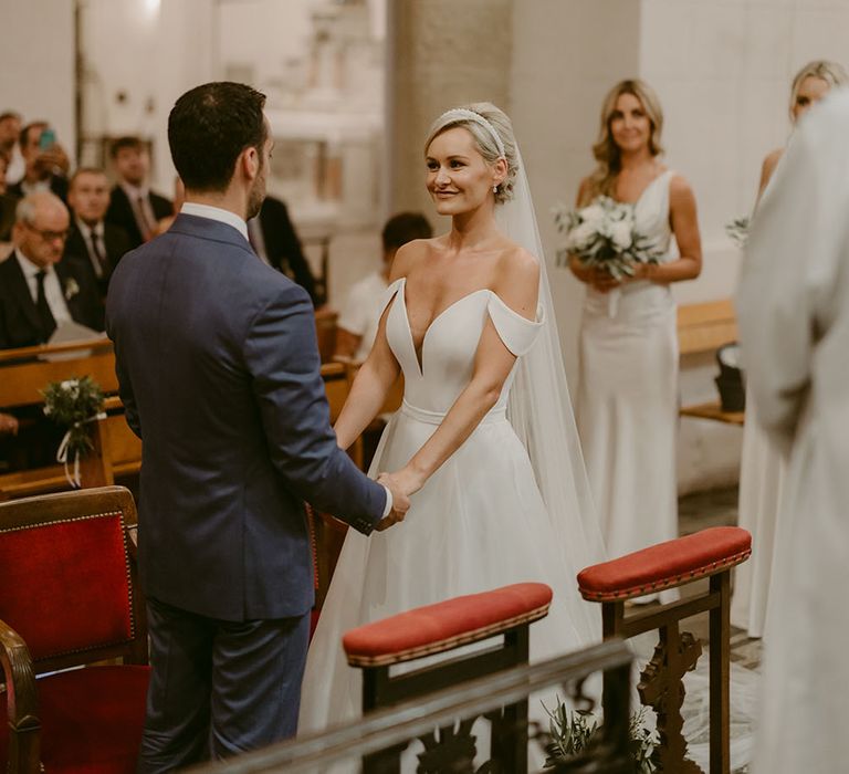 Bride wearing strapless Suzanne Neville wedding dress stands before her groom during church wedding in the South of France