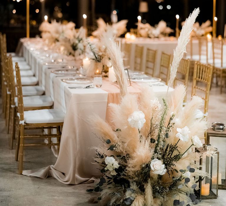 Pampas grass bouquet with neutral tones sits to the end of table for outdoor reception in Phuket surrounded by hanging festoon lighting