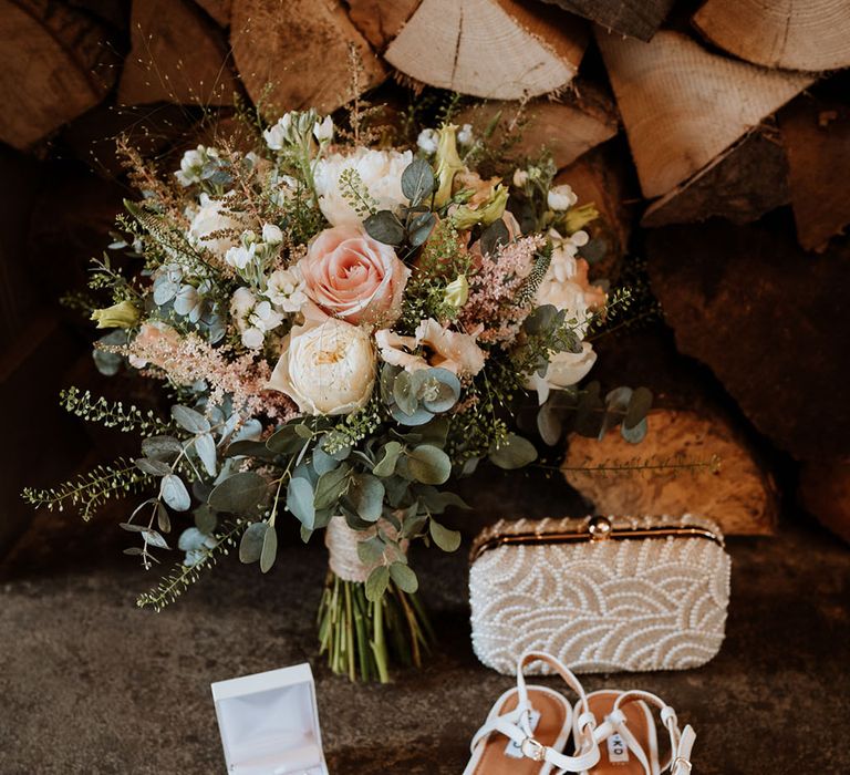 Pastel floral bridal bouquet beside pearl clutch and white strappy heels 