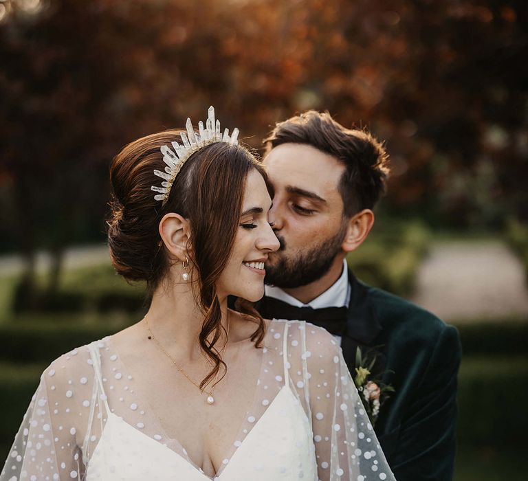 The bride wears pearl jewellery with a quartz crystal crown accessory with the groom in a velvet jacket 