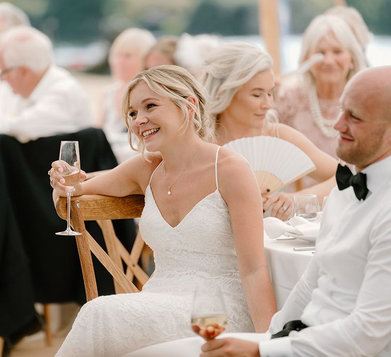 Bride wearing fitted lace wedding dress sits beside her groom during outdoor wedding reception 