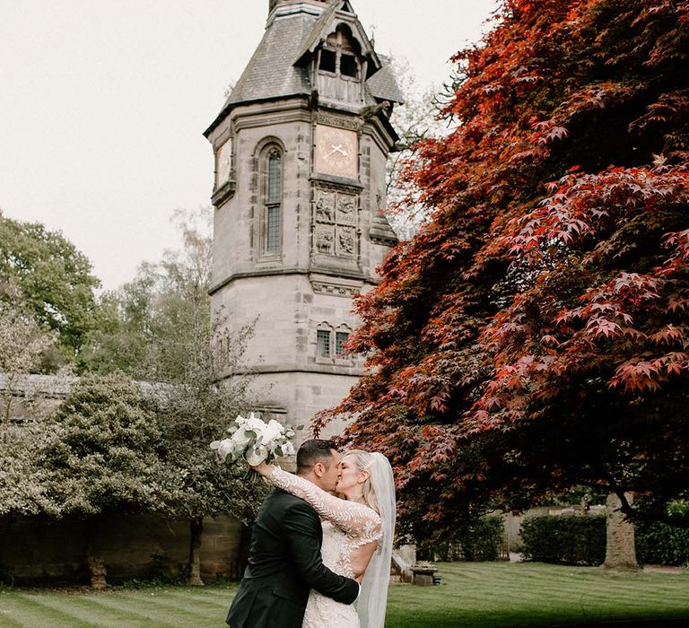 Bride wearing floral embellished wedding dress kisses her groom outside at Hampton Manor