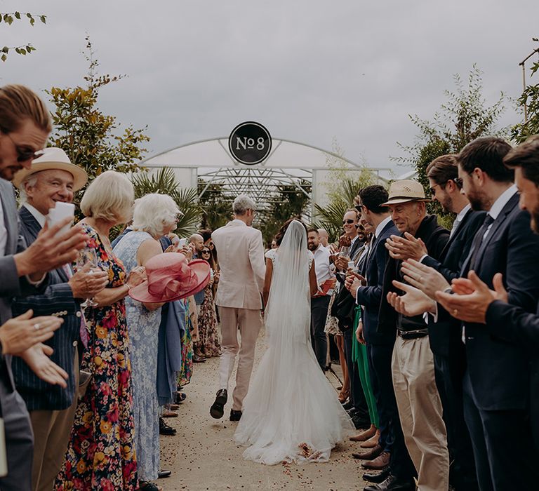 Bride and Groom walk between clapping guests towards Architectural Plants venue