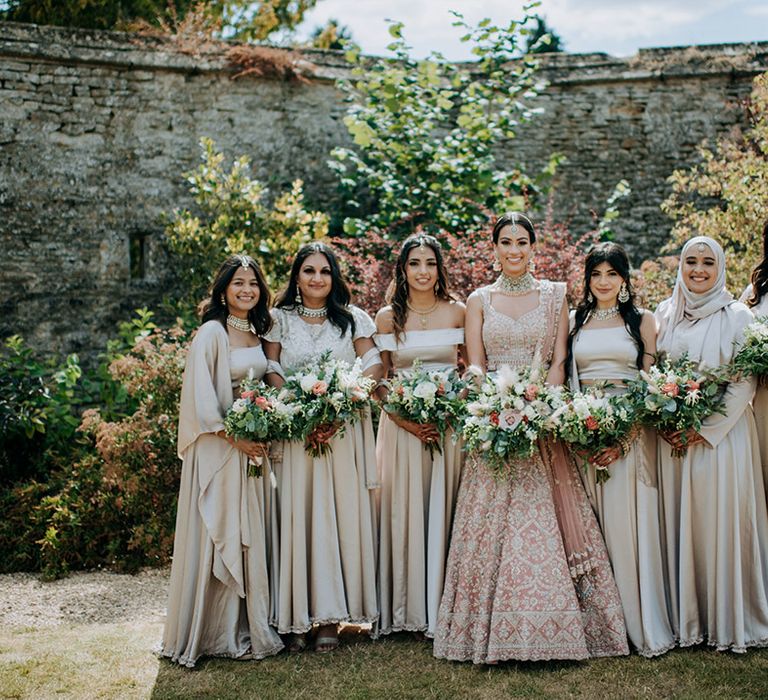 Bride in golden bridal Lehnga poses with bridesmaids in champagne bridesmaid dresses and champagne bouquets in bridemaid's photo