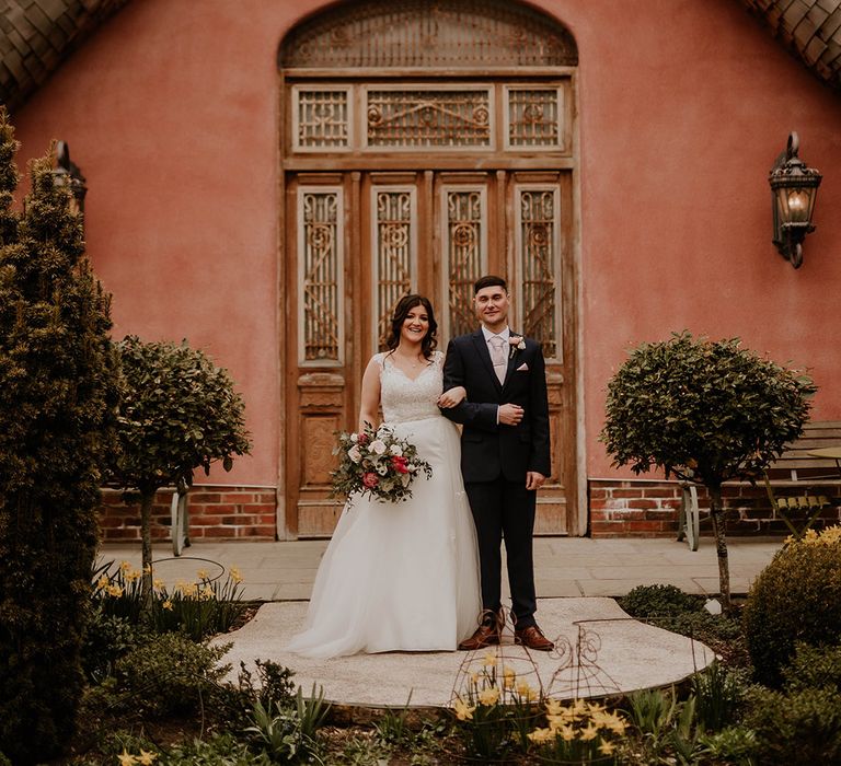 Bride in lace wedding dress stands beside her groom in blue suit and pale pink tie at Le Petit Chateau 