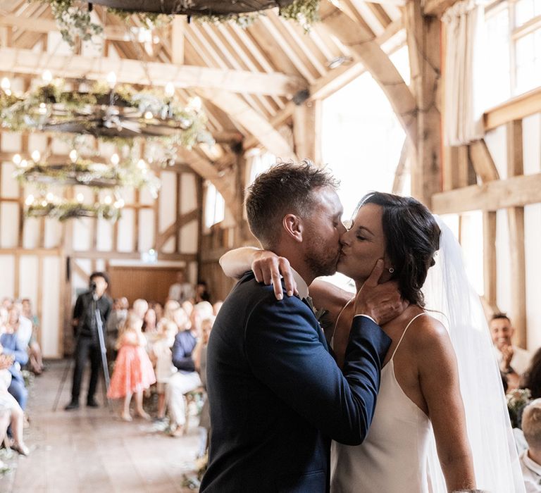 Bride in Grace Loves Lace wedding dress kisses her groom during rustic barn civil ceremony 