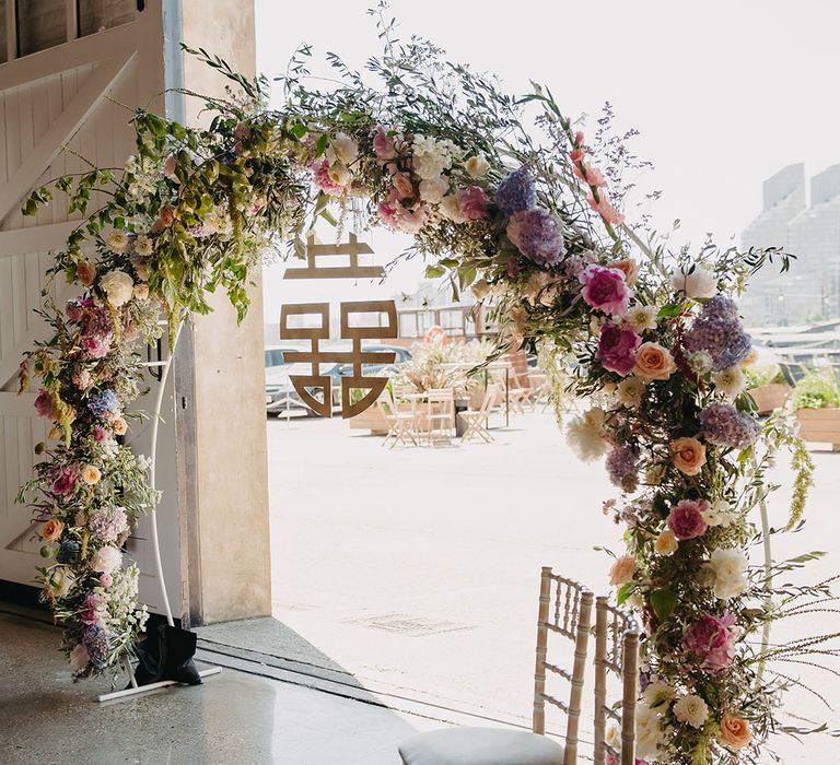 Chinese double happiness sign hangs from pastel floral arch 