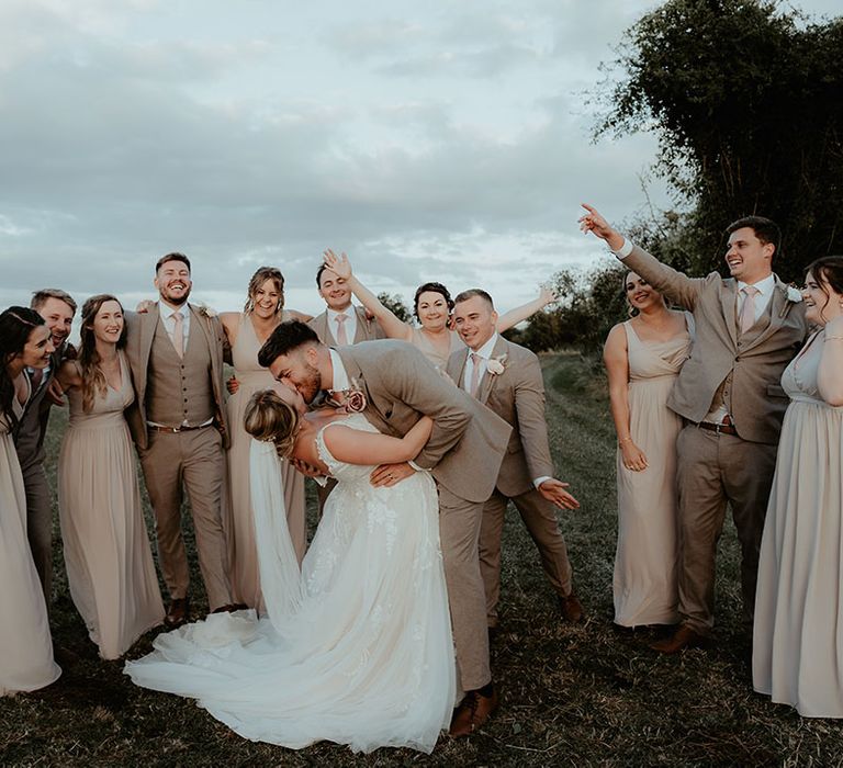 Bride & groom kiss surrounded by groomsmen wearing neutral suits and bridesmaids wearing dusty pink bridesmaid dresses 