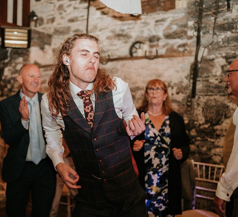 Groom in dark grey checkered waistcoat with burgundy flower patterned tie dancing to live wedding music at boho wedding 