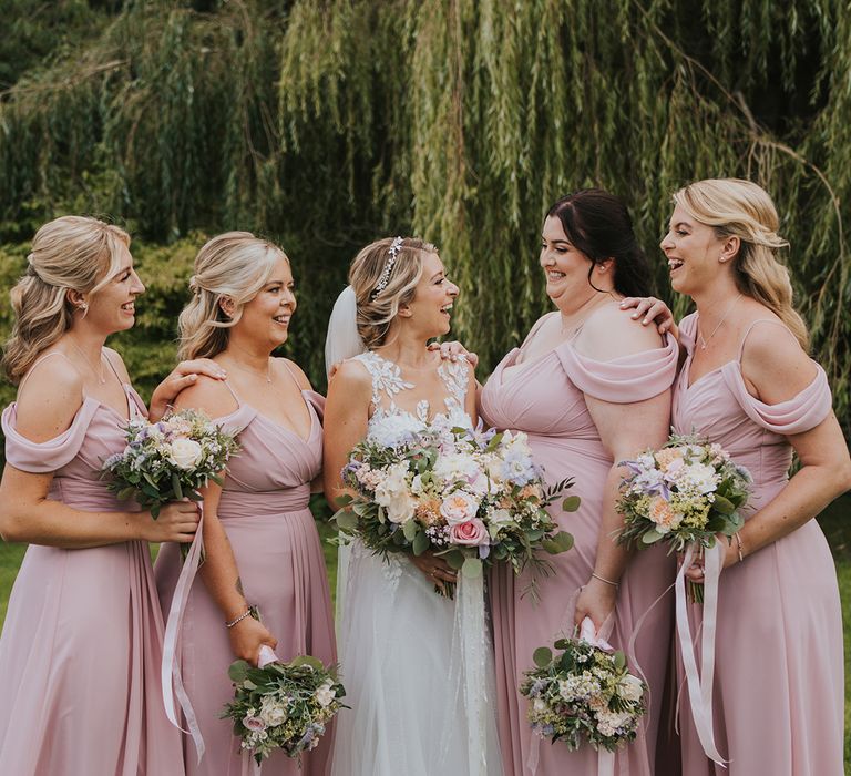 Bridesmaids in pink off the shoulder bridesmaid dresses with the bride in a lace and tulle wedding dress 