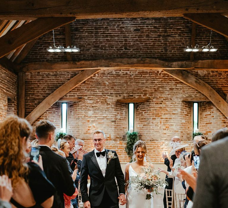 Elms Barn weddings with the bride in a satin wedding dress with the groom in a black tuxedo and dried buttonhole