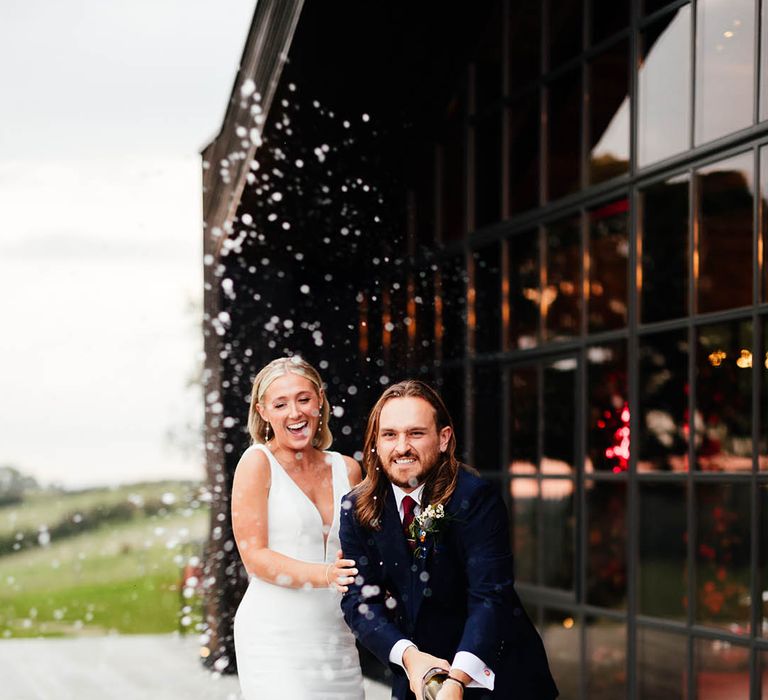 Bride and groom pop champagne together to celebrate their autumn wedding 