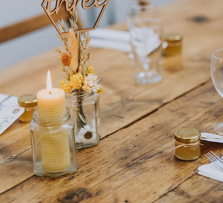 Small glass vases with dried flowers and a wooden laser cut wedding table number sign 