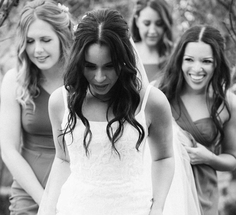 Bridesmaids in mismatched bridesmaid dresses walking with bride in a-line tulle wedding dress with beaded lace applique with petals and a square neckline with side tulle cutouts at South Farm wedding