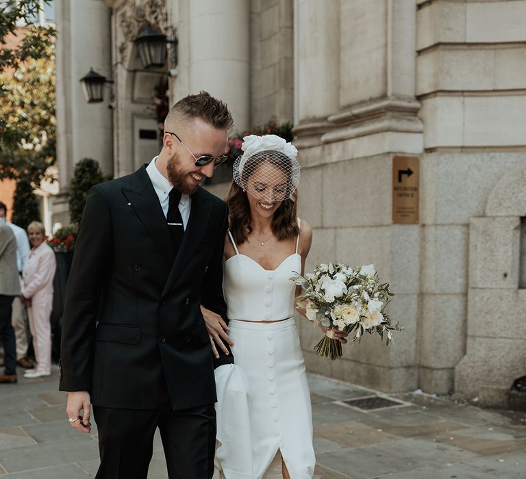 stylish Chelsea wedding with bride in skirt, top and headband and groom in a black suit 