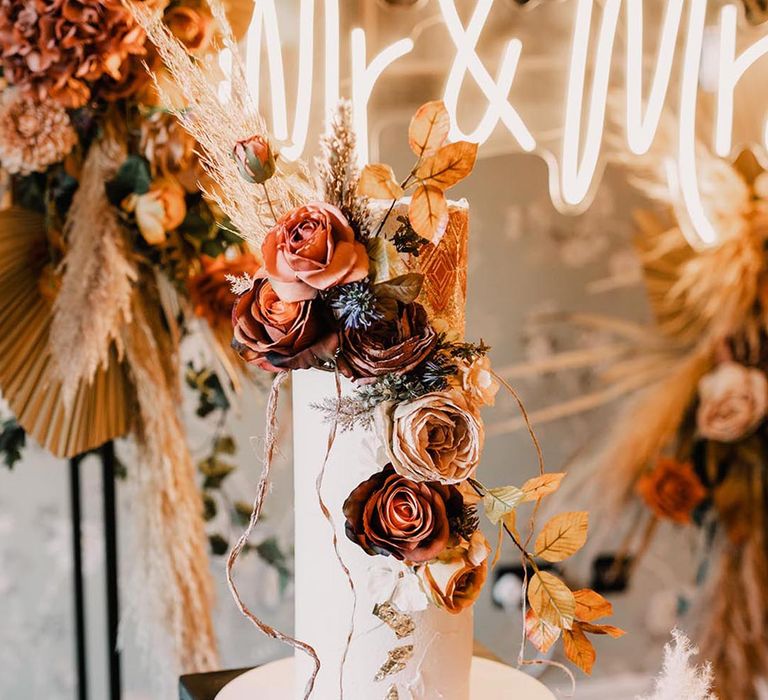 Tall three tier white iced wedding cake with autumnal wedding flowers and neon sign