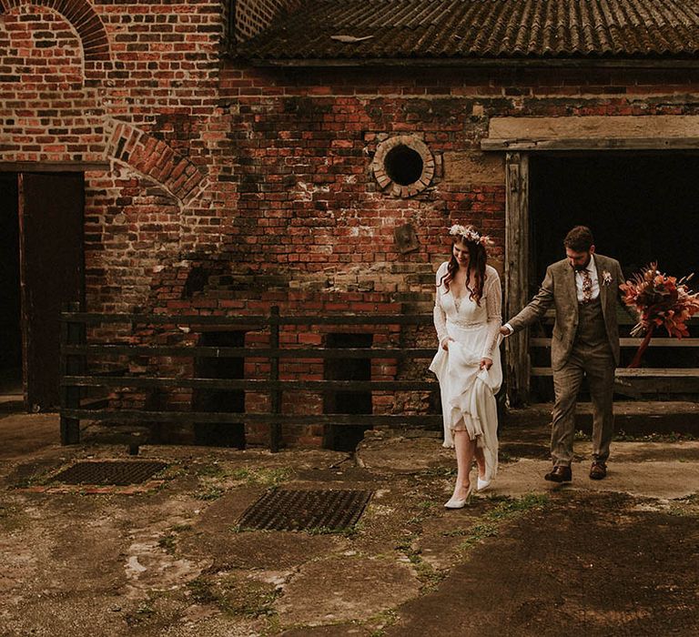 Bride wearing a boho flower crown and lace wedding dress with the groom in a three piece brown suit carrying pink dried flower bouquet with pampas grass