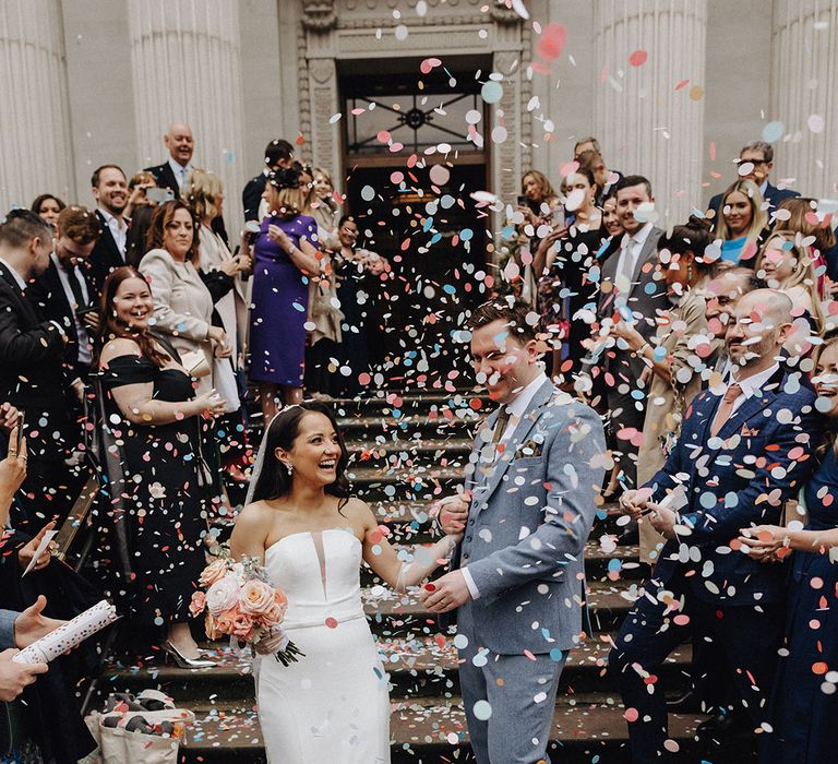 Colourful pastel confetti moment as the bride and groom exit their ceremony as a married couple 