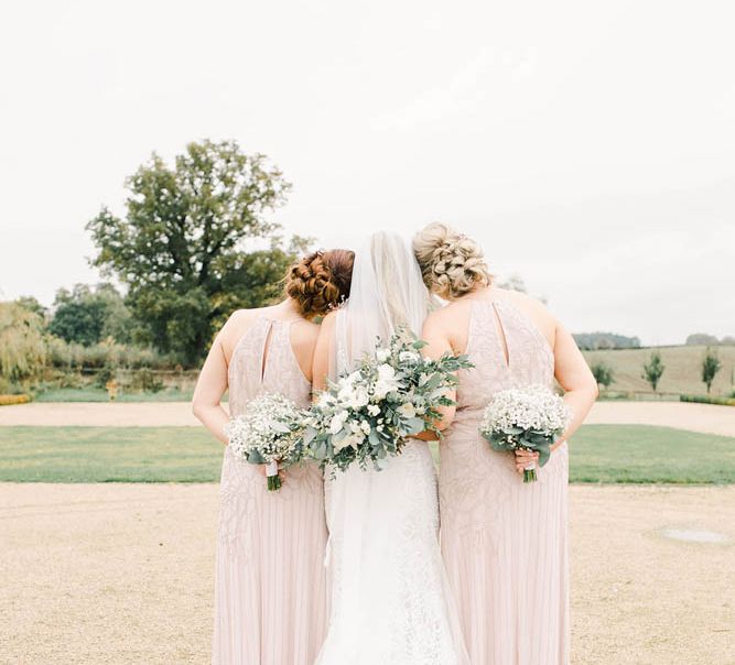 Bride and bridesmaids embracing with their bouquets behind their backs 