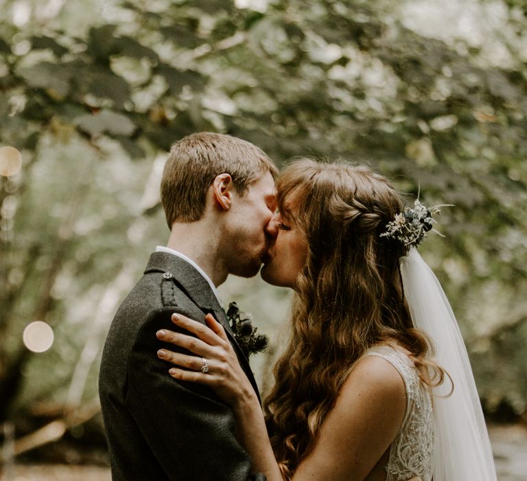 The married couple share a kiss in a forest in the Scottish Highlands for their elopement