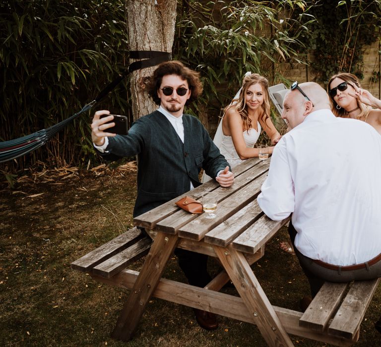 wedding guests sitting on a picnic table outside 