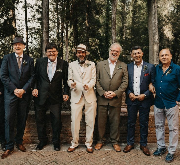 The groom and groomsmen line up in neutral toned olive green and blue suits