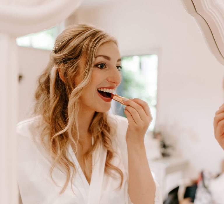 Bride with half up half down wedding hairstyle putting on her lipstick