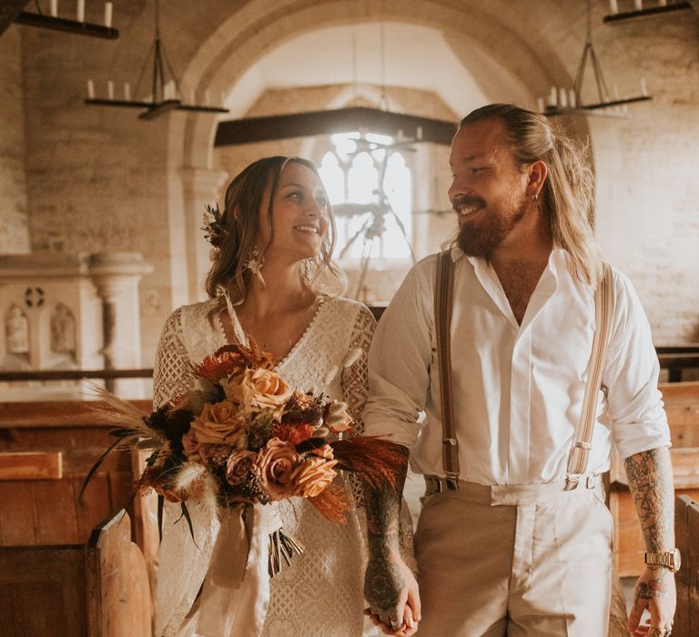 Bride & groom walk down the aisle with bride holding Autumnal bouquet 