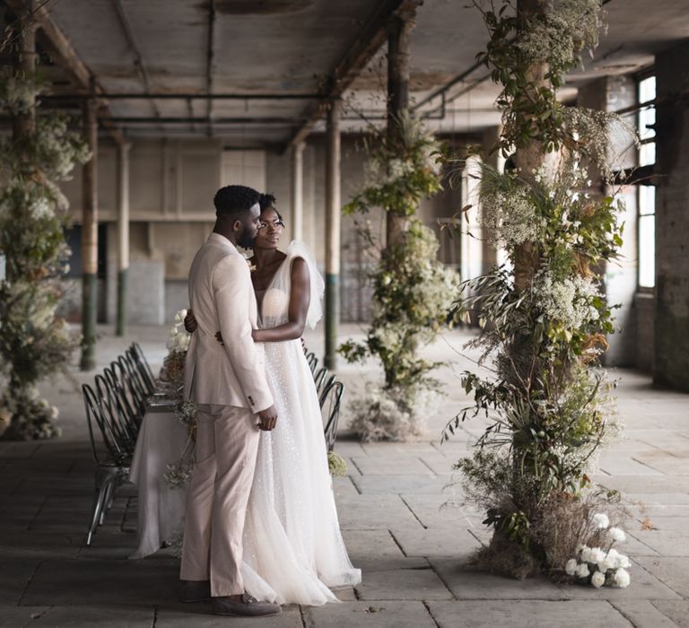 Bride and groom standing in an industrial wedding venue with green and white flower pillars 