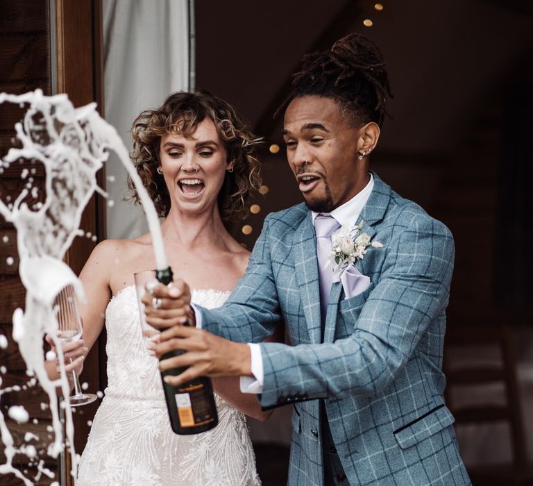 The bride and groom pop champagne in the outdoor cabin at Sedgewell Barn