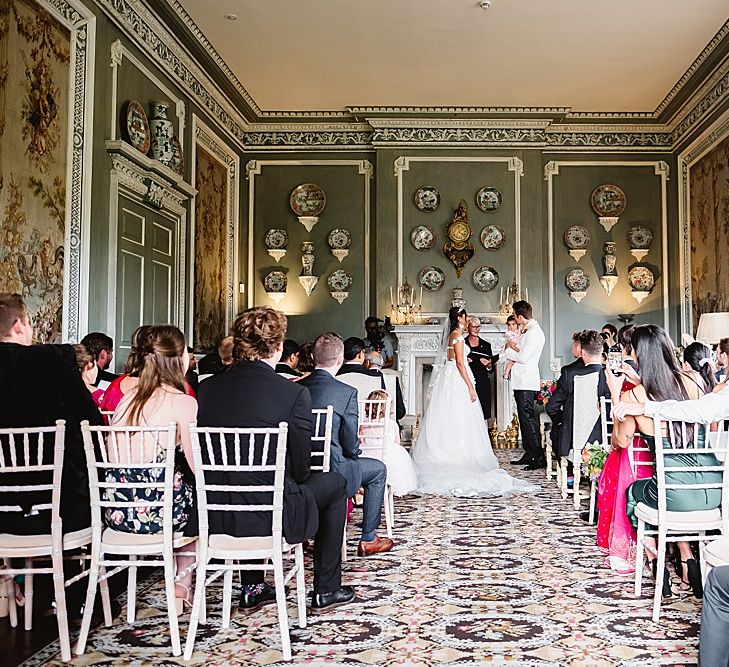 Bride in a princess wedding dress and groom in a tuxedo standing at the altar with their daughter exchanging their wedding vows 