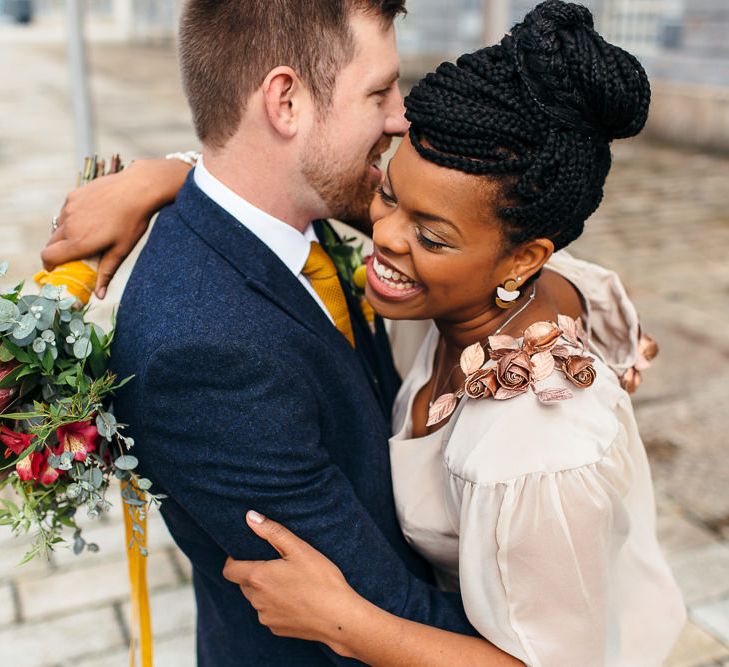 A Black bride wears her braids in a high bun. She is laughing with her new husband and wears a cape.