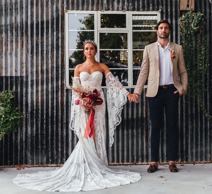 Bride & groom stand together outside rustic barn 