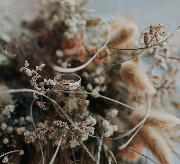 Silver wedding ring nestled in dried flower bouquet 