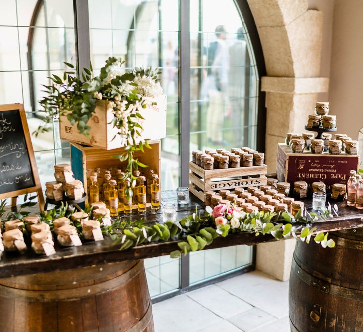 A table of wedding favours at a wedding. The table top sits on two big barrels and there are jams and drinks on top of the table. Photography by John Barwood.