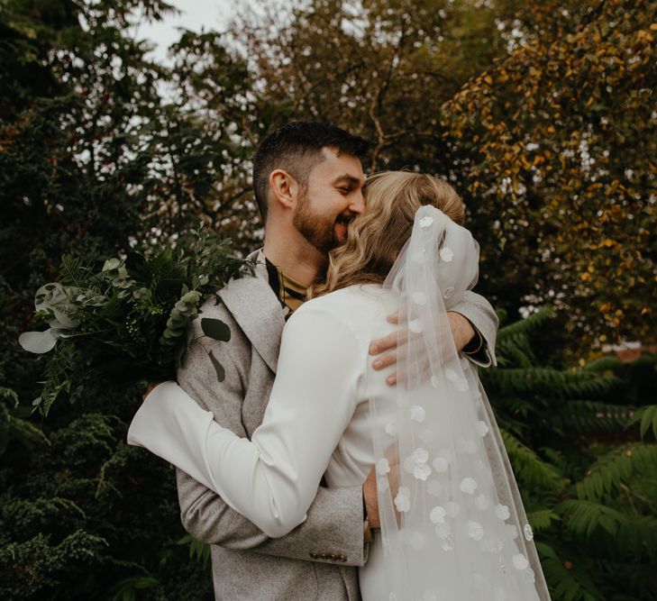 Groom embracing his bride in a appliqué wedding veil