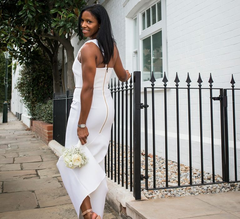 Stylish bride in a fitted Roland Mouret dress with one shoulder and zip back detail holding a white rose bouquet and wearing Christian Louboutin shoes 