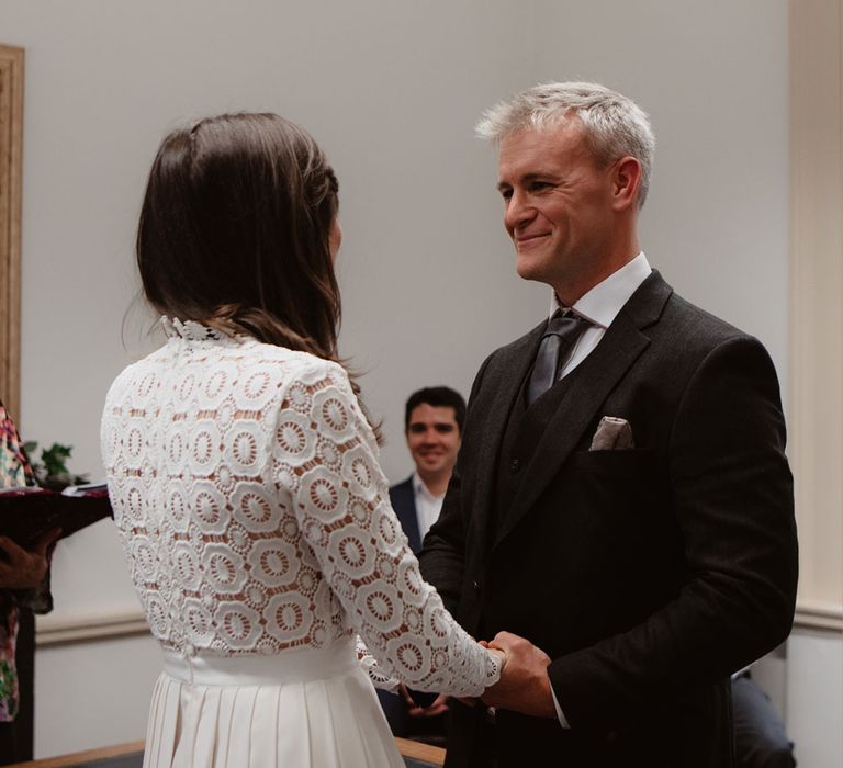 Groom in brown woollen blazer and waistcoat smiles at bride in Self Portrait wedding dress inside Bristol Registry office