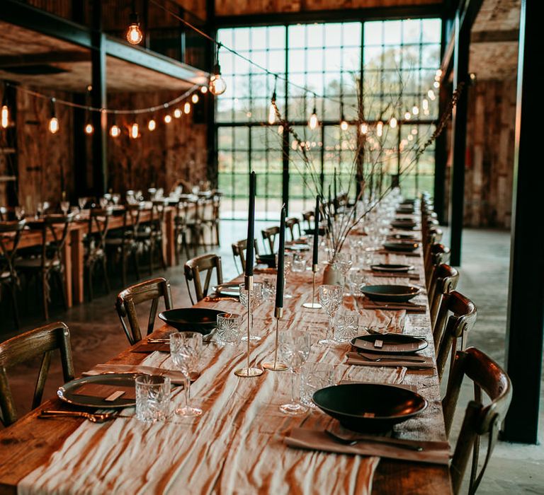 Wooden table at wedding reception decorated with fabric table runner, taper candles and dried grasses 