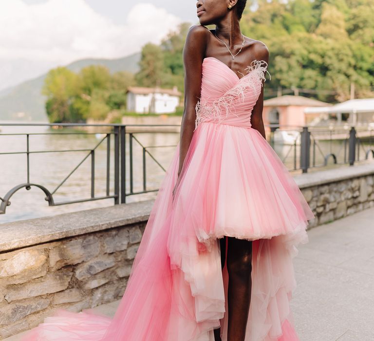 Black bride stands beside Lake Como in Italy whilst wearing pastel pink wedding gown with tulle skirt 