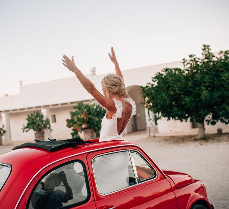 The bride standing up through the sun roof of the Fiat 500 wedding car