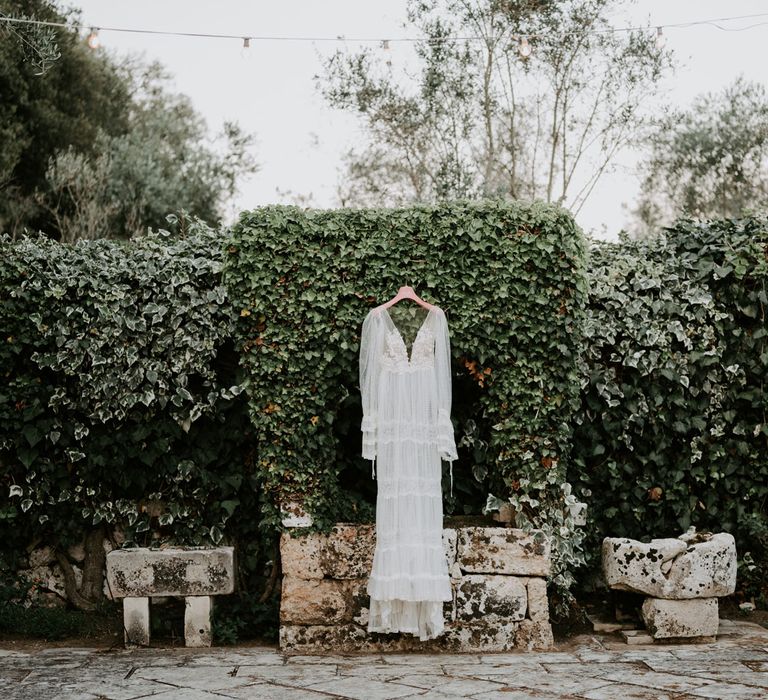 Long-sleeved boho wedding dress with lace and mesh detailing hanging in garden at enchanted forest wedding in Italy