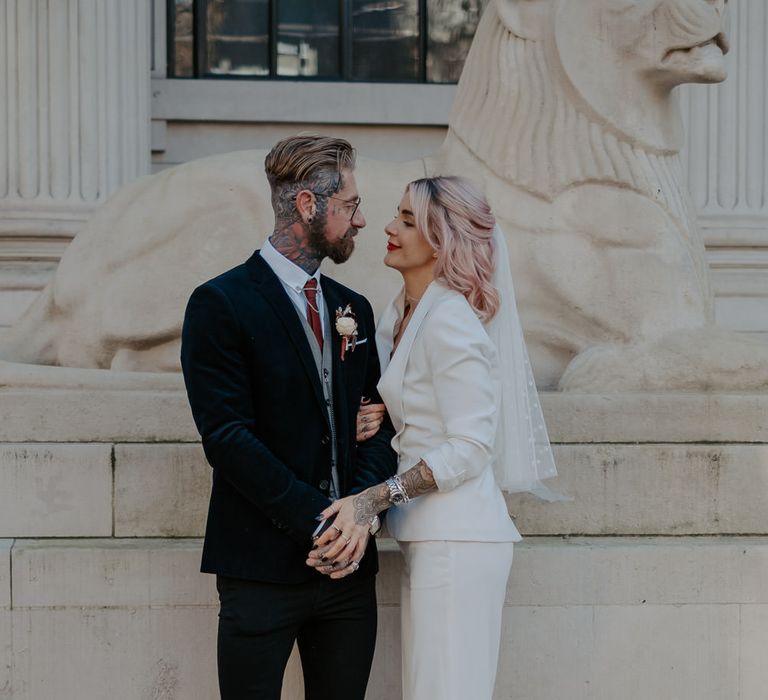 Bride and groom stand close together facing each other in front of lion statue at Marylebone wedding