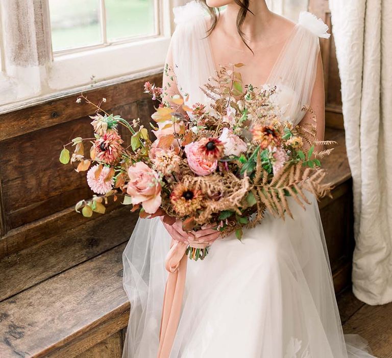 Classic bride with a low bum and wavy sides looking our the window holding her Autumn bouquet 